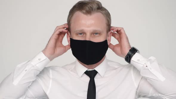Young Bearded Guy Applies Protective Mask To His Face and Poses for Camera in White Interior.