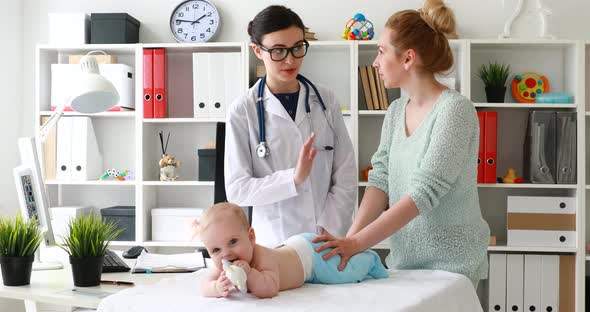 Mom with Doctor Examining Baby Lying and Playing on Table and Discussing Treatment.