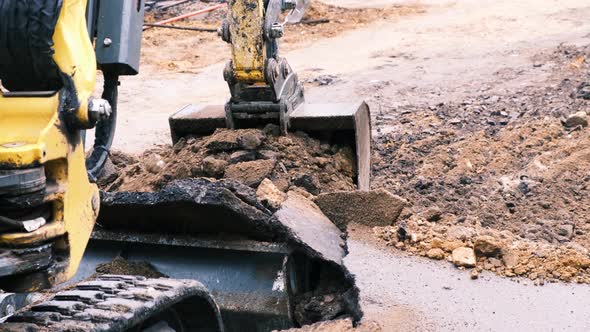 Excavator Bucket Picks Up Broken Asphalt and Earth