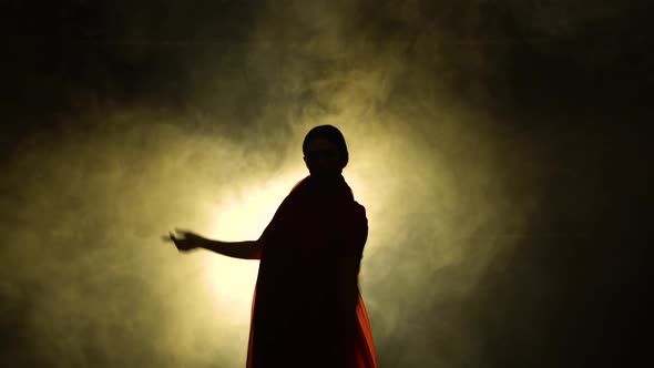 Silhouette a Young Girl Dancer in a Red Sari. Indian Folk Dance. Shot in a Dark Studio with Smoke alt