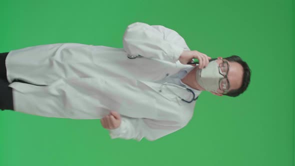 Asian Doctor With Stethoscope Wearing Mask, Talking On Mobile Phone While Running On Green Screen alt