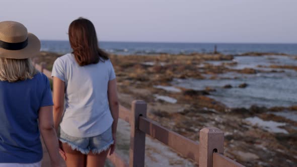Mother and daughter walking down the wooden pier by the sea at sunset alt