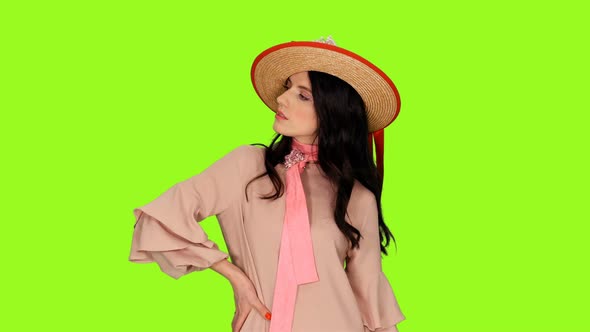 Charming Young Brunette Woman in Pink Dress and Straw Hat Posing on Green Background