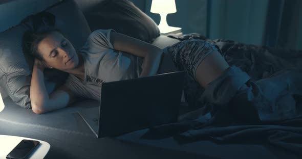 Woman lying in bed and connecting with her laptop late at night, she can't sleep