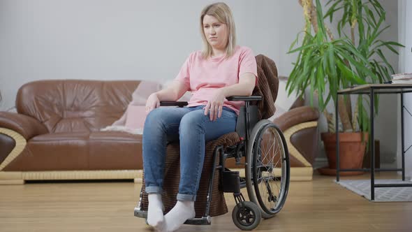 Wide Shot Portrait of Depressed Frustrated Disabled Woman Sitting in Wheelchair at Home Thinking alt