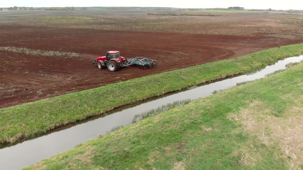 Farmer on a Tractor Cultivates Farmland with a Disc Harrow Near a Small Reclamation River alt