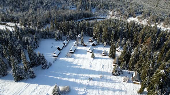 Aerial view of snow capped huts in the mountains, surrounded by spruce forest covered with snow