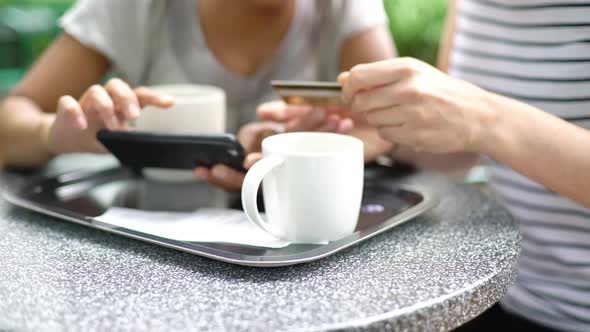 Women using credit card and smartphone to make a payment online in outdoor cafe
