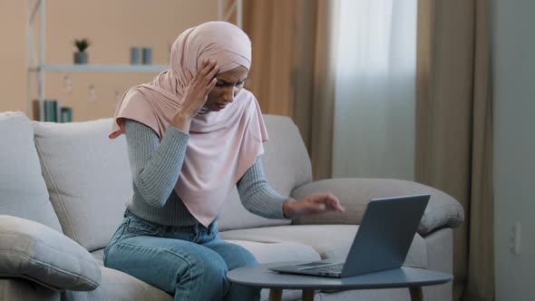 Young Muslim Woman in Pink Hijab Sitting on Sofa Working Using Laptop Having Headache Migraine Sad alt