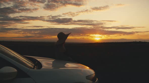 Female Leaning On A Car At Sunset