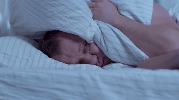 Lying in bed at night, a man cannot sleep, covers his head with a pillow alt