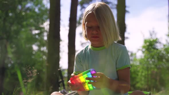 Blonde Boy Sitting in the Park and Plays Popit Rainbow Colors