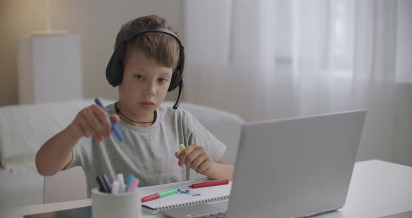 Little Boy Is Using Laptop and Headphones and Drawing By Colored Pencils at Home, Happy Childhood alt