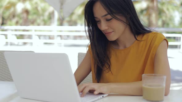 Adorable Mixed Race Woman Sitting at Outdoor Cafeteria Table and Using Laptop alt