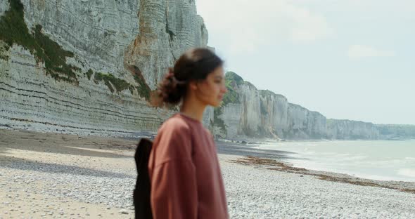 A Young Woman Walks Along a Pebbly Beach Past Sheer Chalk Cliffs alt