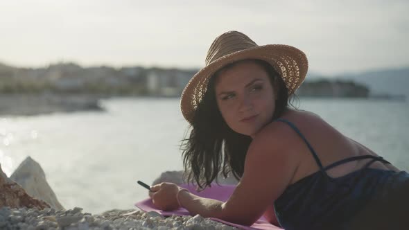 Girl with a Phone Sunbathes By the Sea alt