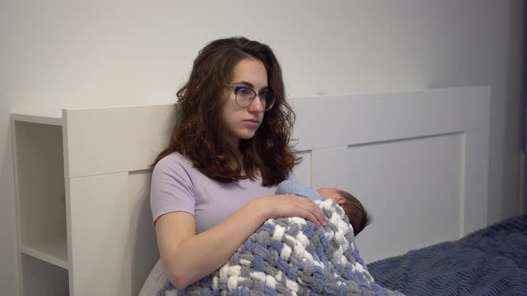 An Exhausted Young Mother Cradles a Child in Her Arms in Bed alt