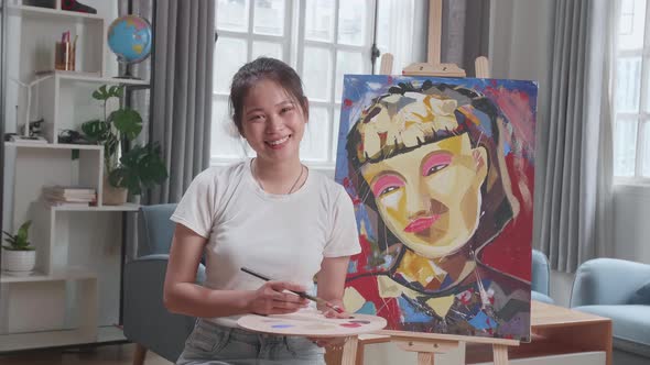 Asian Artist Girl Sitting And Holding Paintbrush  And Smiling After Finish Painting alt
