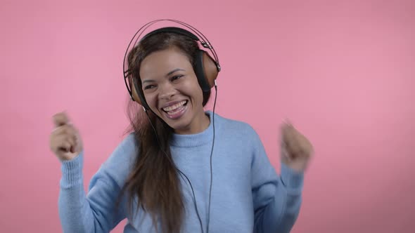 Mixed Race Woman Dancing Funny with Headphones Isolated on Pink Studio Background alt