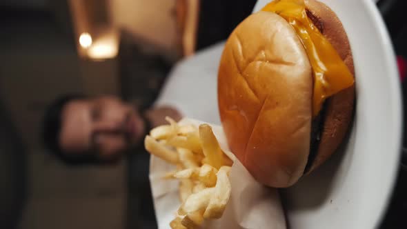 A Man Eats French Fries Next to a Fast Food Cheeseburger on a White Plate