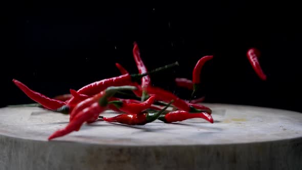 Slow Motion of Red Chili Peppers Dropped Down into Cutting Board, then Scattered. alt