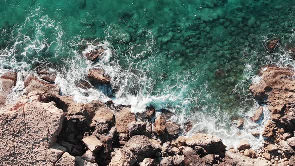 Aerial top view of sea coast line with ocean waves hitting rocky seashore creating white foam  alt