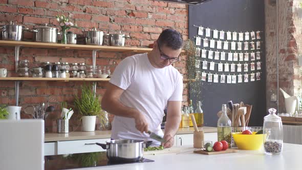 Man Cuts Vegetables in the Kitchen and Experiences a Sharp Headache He Grabs His Head alt