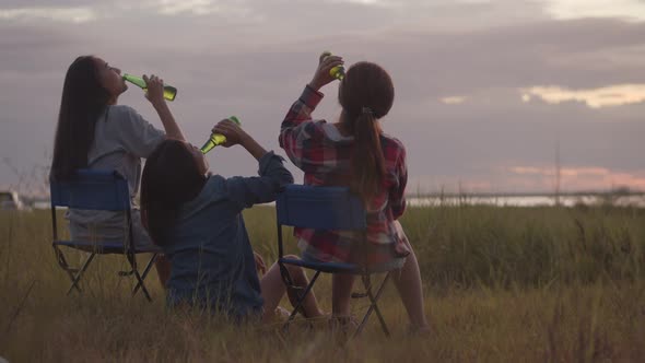 Asian women sitting on a chair with friends camping in nature having fun together drinking beer.