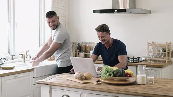 Happy gay male couple talking together in kitchen while doing daily morning routine