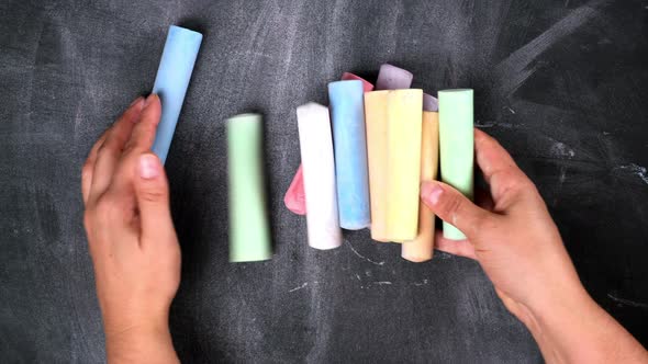 female hand puts a stack of colored crayons for drawing on a black surface, top view alt