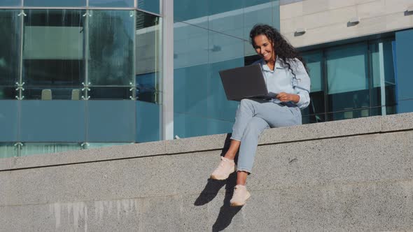 Long Shot Smiling Happy Young Business Woman Freelancer Girl Student Sitting on Street City Building alt