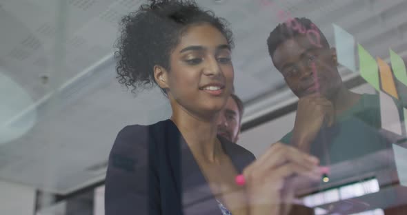 Diverse colleagues using memo notes and writing on glass wall having a discussion alt