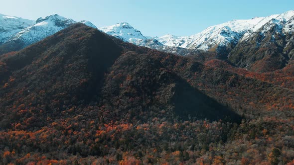Aerial establishing shot of snowy mountains with autumn vegetation on base in Chile alt