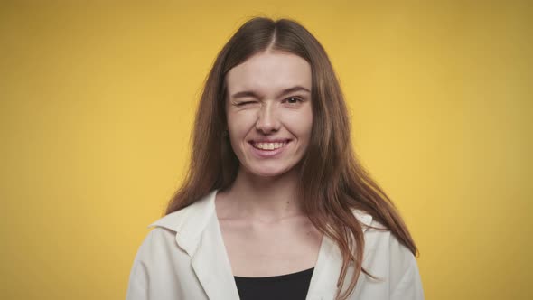 Young Adult Caucasian Woman is Winking and Smiling on a Bright Yellow Background alt