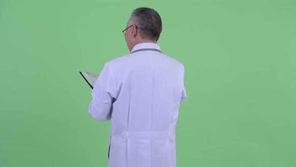 Rear View of Happy Mature Japanese Man Doctor Checking with Clipboard alt