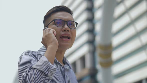 Asian men with glasses use phones in street near big office buildings.