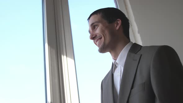 Young Successful Happy Laughing Businessman Standing in Front of Windows Looking Into Distance on