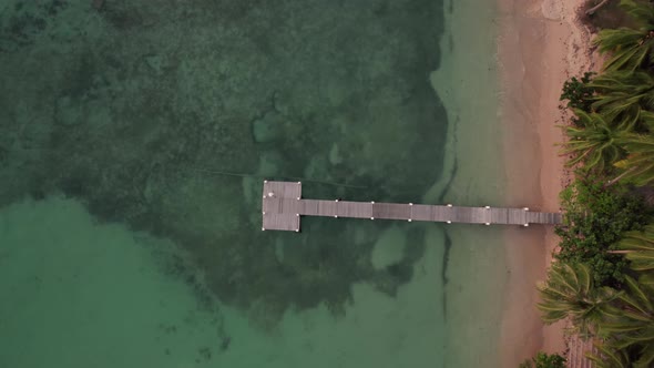 Drone Descending Down Towards Pier Over Sea From Beach alt