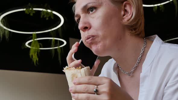 a Caucasoid Woman with a Wary Expression Chews a Doner Kebab and is Silent While Listening to Her