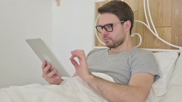 Beard Young Man Celebrating Success on Tablet in Bed alt
