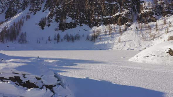Aerial View of Frozen Lake Snow Land in Mountain Feet. Forest Growing in mountain.Drone Point of alt