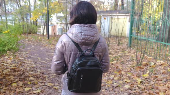 A Brunette with Short Hair in a Brown Jacket Walks in the Park on a Sunny Autumn Day alt
