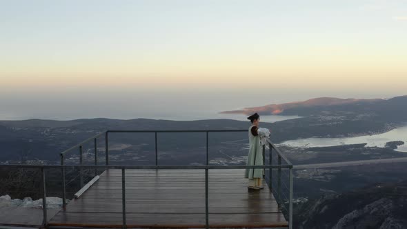Woman in Traditional Montenegrin Dress enjoying glass of red wine standing on wooden deck with birds alt