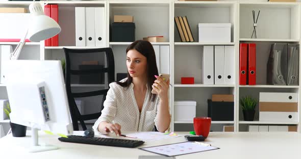Businesswoman Working at Computer and Using Smartphone in Light Office