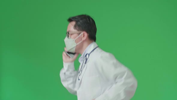 Asian Doctor With Stethoscope Wearing Mask, Talking On Mobile Phone While Running On Green Screen alt
