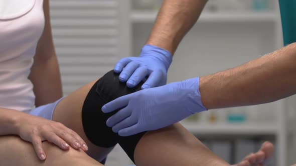 Therapist Touching Patient Leg in Compression Knee Brace, Trauma Rehabilitation