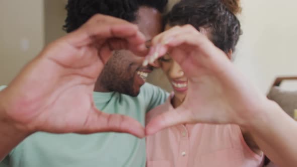 Happy biracial couple gesturing heart sign with hands alt
