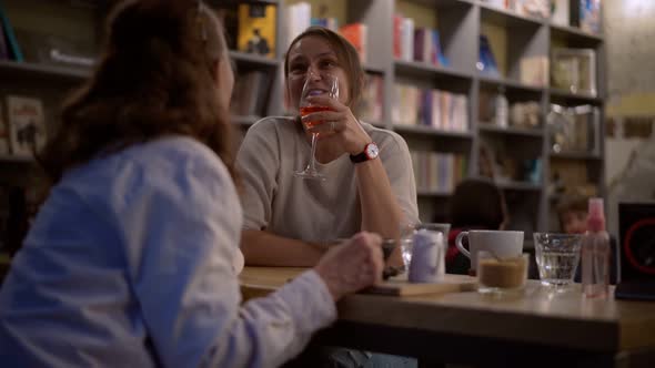 A Mature Adult Woman Sits in a Cafe with Her Adult Daughter in the Evening alt