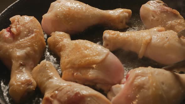 Fry Chicken Drumsticks in a Pan and Turn Over with Culinary Steel Tongs