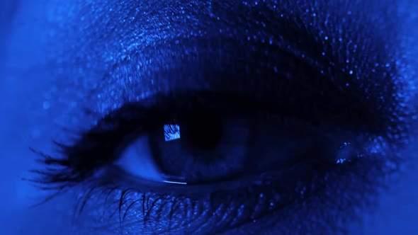 Extreme Closeup of Woman's Opening Beautiful Eye in Dark Red and Blue Lights
